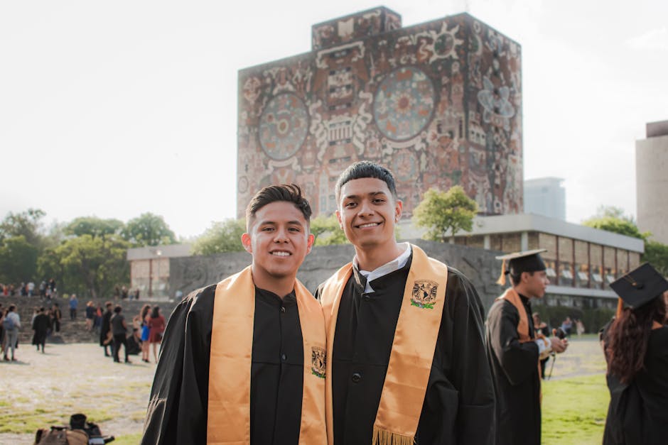Two graduates in gowns pose in front of UNAM Central Library, Mexico City.