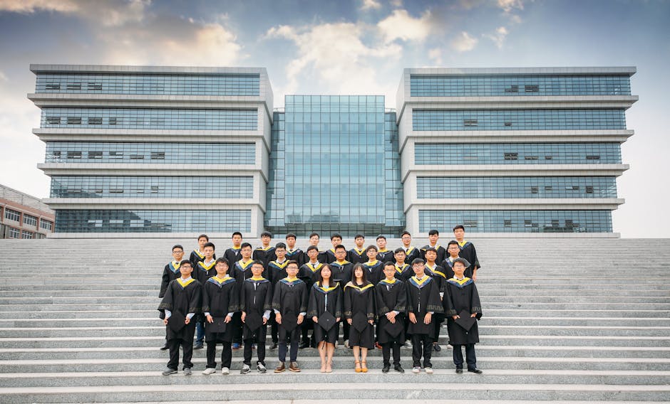 A group of university graduates in gowns posing on campus steps ready to celebrate achievement.